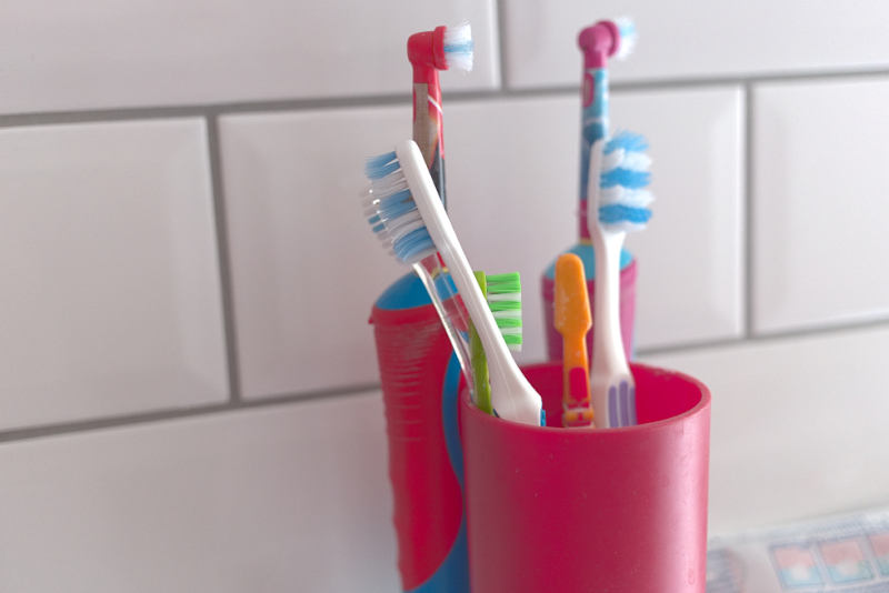 Several manual and electric toothbrushes in a red cup