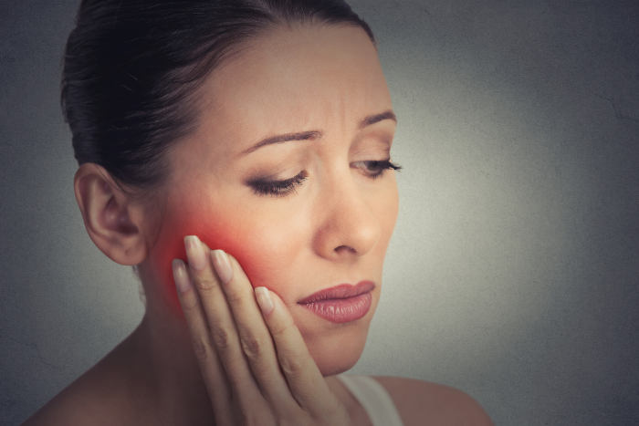 woman experiencing tooth pain Woman holding her cheek with a red highlight on her jaw