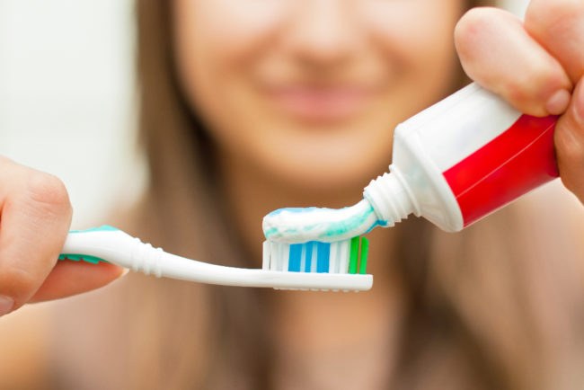 woman pouring toothpaste on a toothbrush