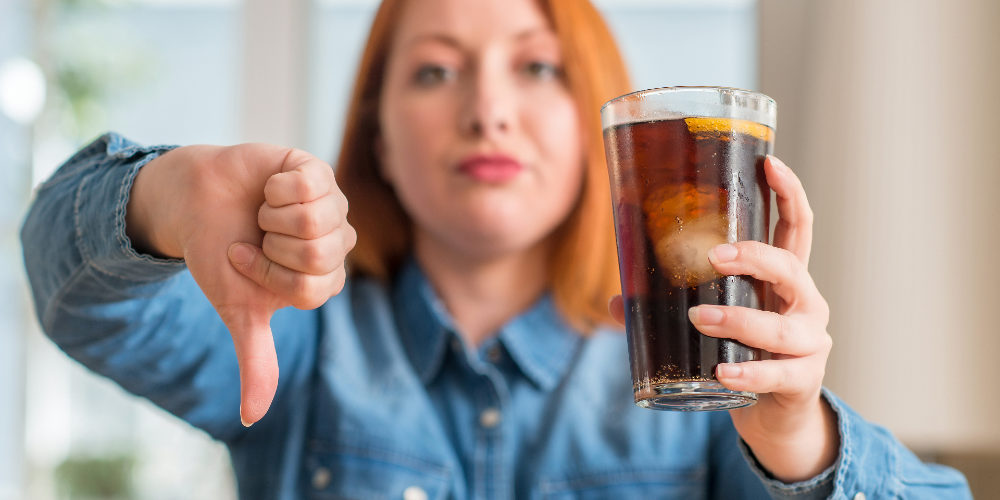 women holding a cup of soda on one hand while the other hands she gives a dumps down