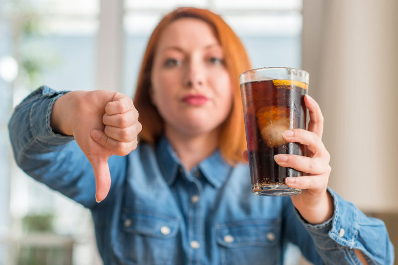 women holding a cup of soda on one hand while the other hands she gives a dumps down Woman holding a glass of soda while giving a thumbs-down