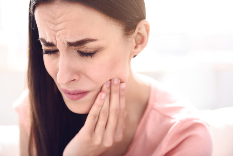 women experiencing a missing tooth ache Woman wincing with a hand held against her jaw