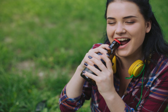 woman opening a bottle cap using her teeth