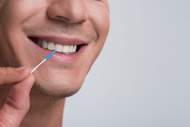 interdental-tooth-pick Man using an interdental brush. How to use interdental brushes and how they differ from traditional floss.