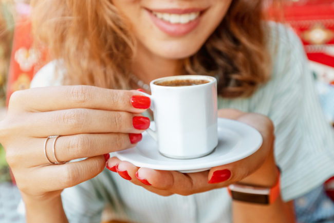 is-coffee-really-bad-for-your-teeth Woman drinking a cup of coffee whilst smiling and enjoying her day.