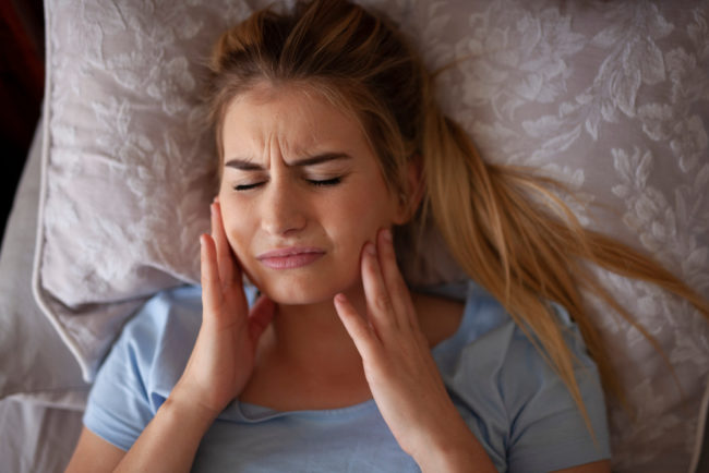 Woman waking up and suffering from teeth grinding pain.