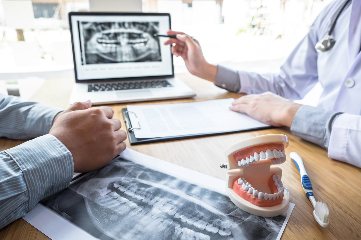 Professional Dentist showing jaw and teeth the x-ray photograph and discussing during explaining the consultation treatment issues with patient and writing history list on report.
