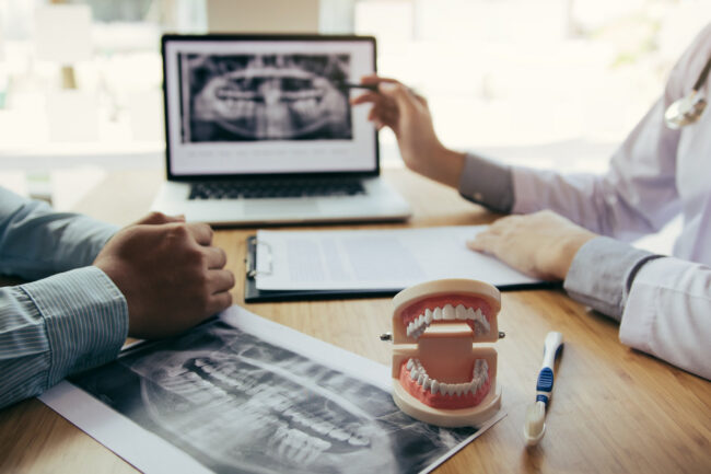Dentists are discussing dental problems at report x-ray image on Dentists are discussing dental problems at report x-ray image on laptop screen to patients.