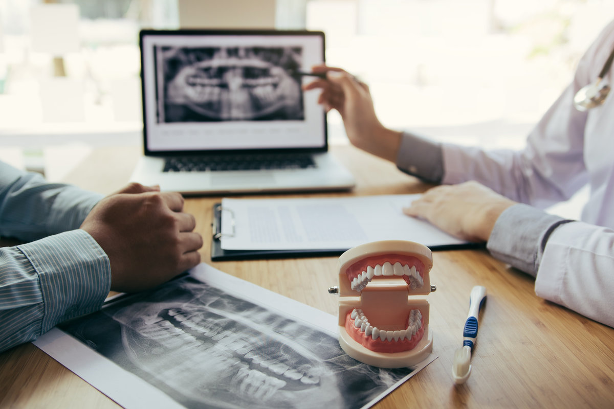 Dentists are discussing dental problems at report x-ray image on Dentists are discussing dental problems at report x-ray image on laptop screen to patients.