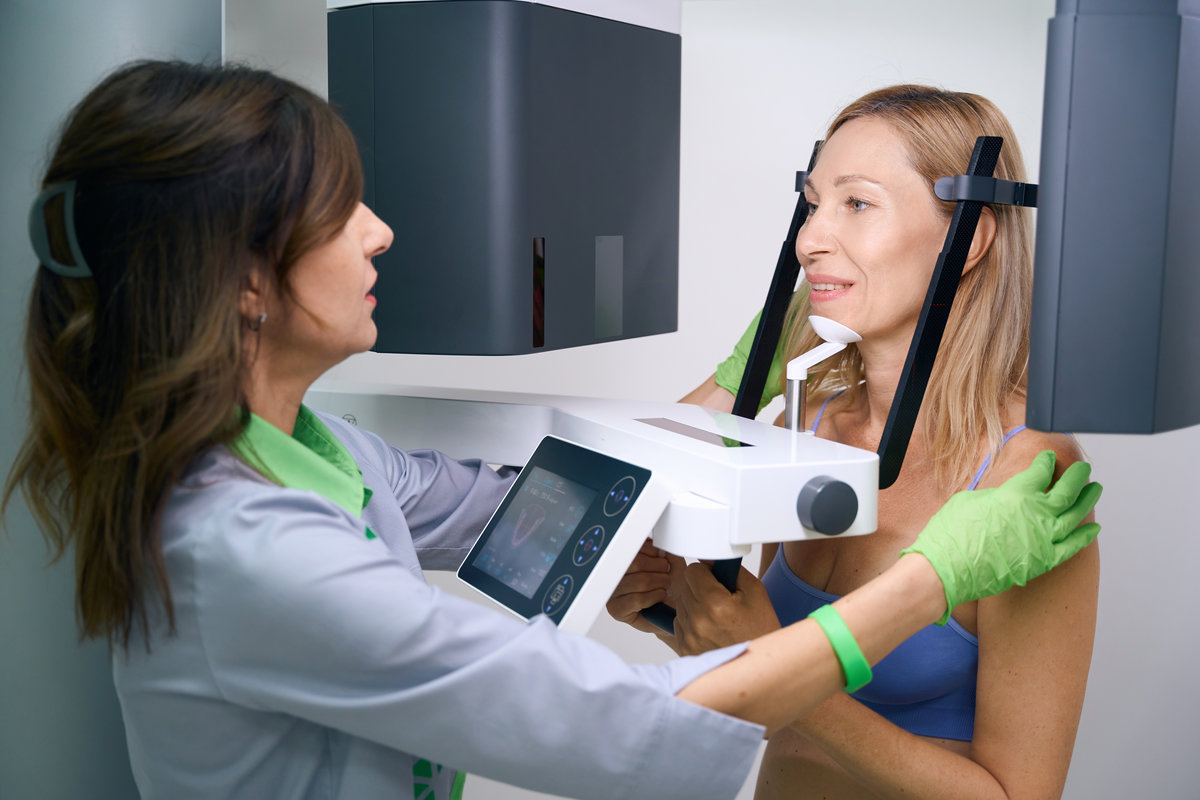 Radiographer preparing woman for 3D CBCT scan in dentistry clinic Experienced radiologic technologist positioning adult female patient inside dental cone-beam computed tomography scanner