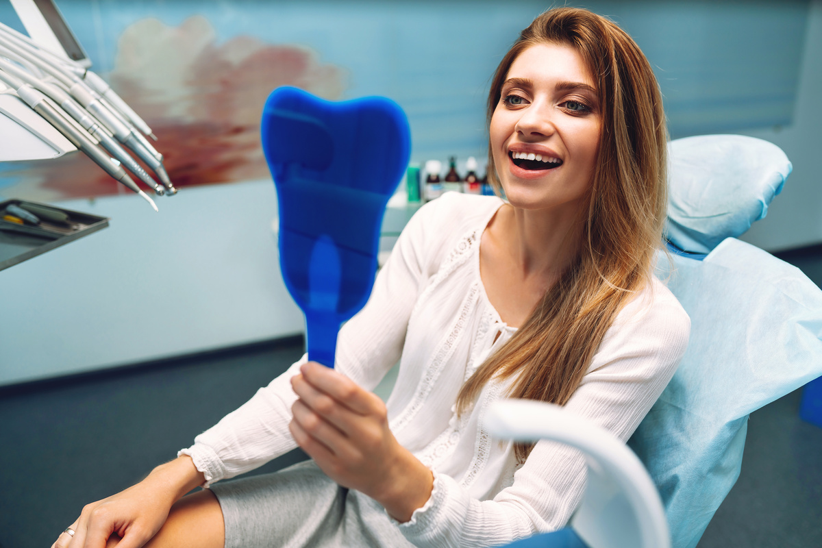 Smiling woman at reception in dental clinic during procedure. Patient at dentist examines teeth in modern clinic. Overview of caries prevention. Medicine concept. Healthy teeth.