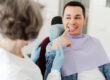 Young attractive male patient sitting in dental chair pointing at teeth, having pain, talking with professional dentist doctor in modern dental clinic. Concept of dental care, health care