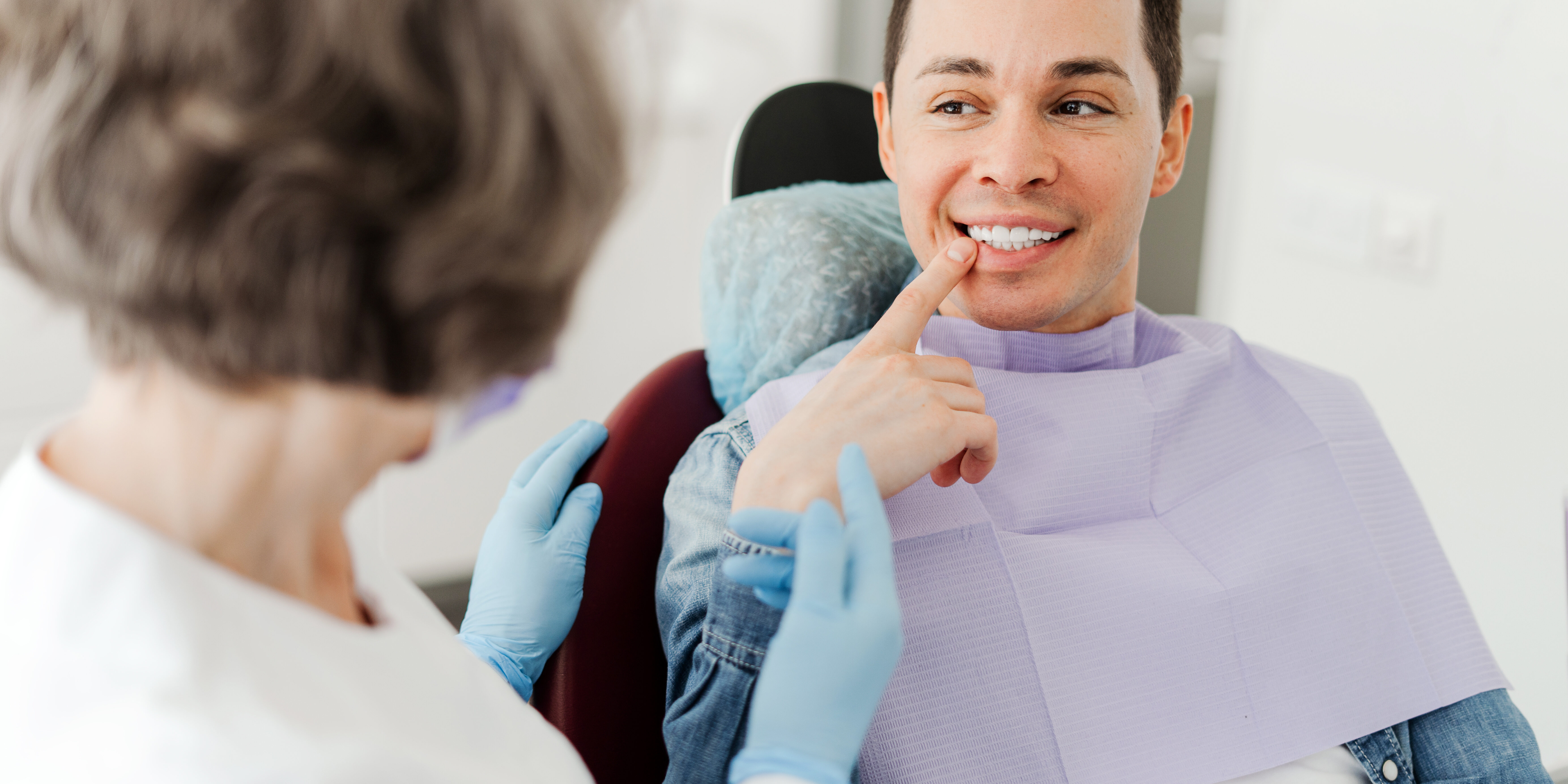 Male patient sitting in dental chair pointing at teeth, talking with professional dentist doctor Young attractive male patient sitting in dental chair pointing at teeth, having pain, talking with professional dentist doctor in modern dental clinic. Concept of dental care, health care