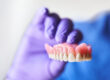 Dentist with purple gloves holding dentures in hand. Concept of dental prosthesis and dental health.