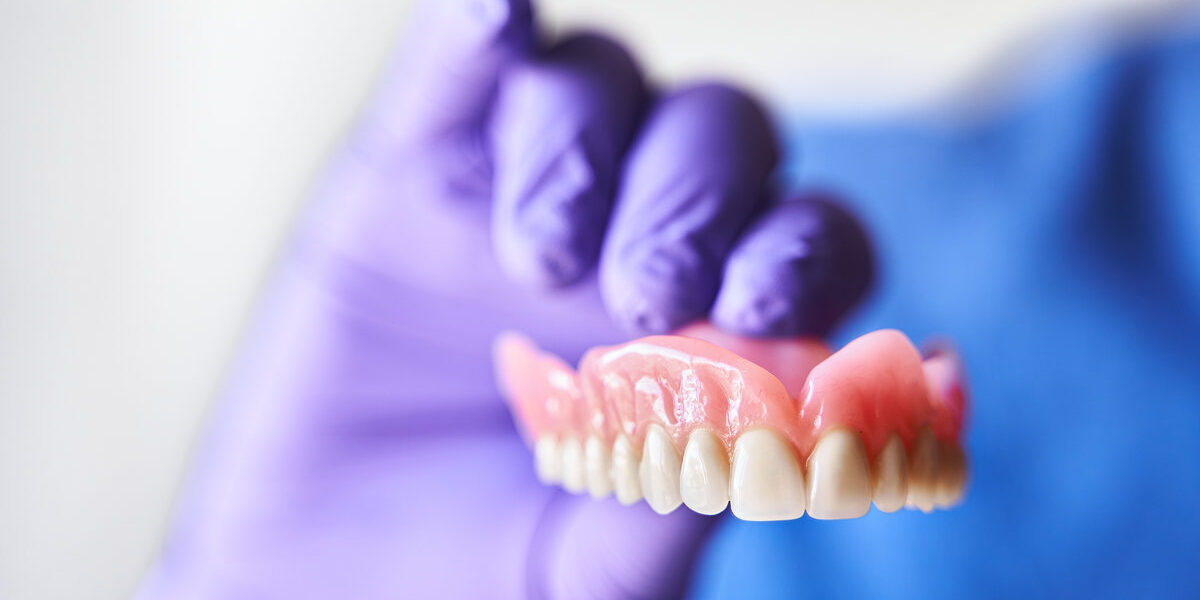 Dentist with purple gloves holding dentures in hand. Concept of dental prosthesis and dental health.