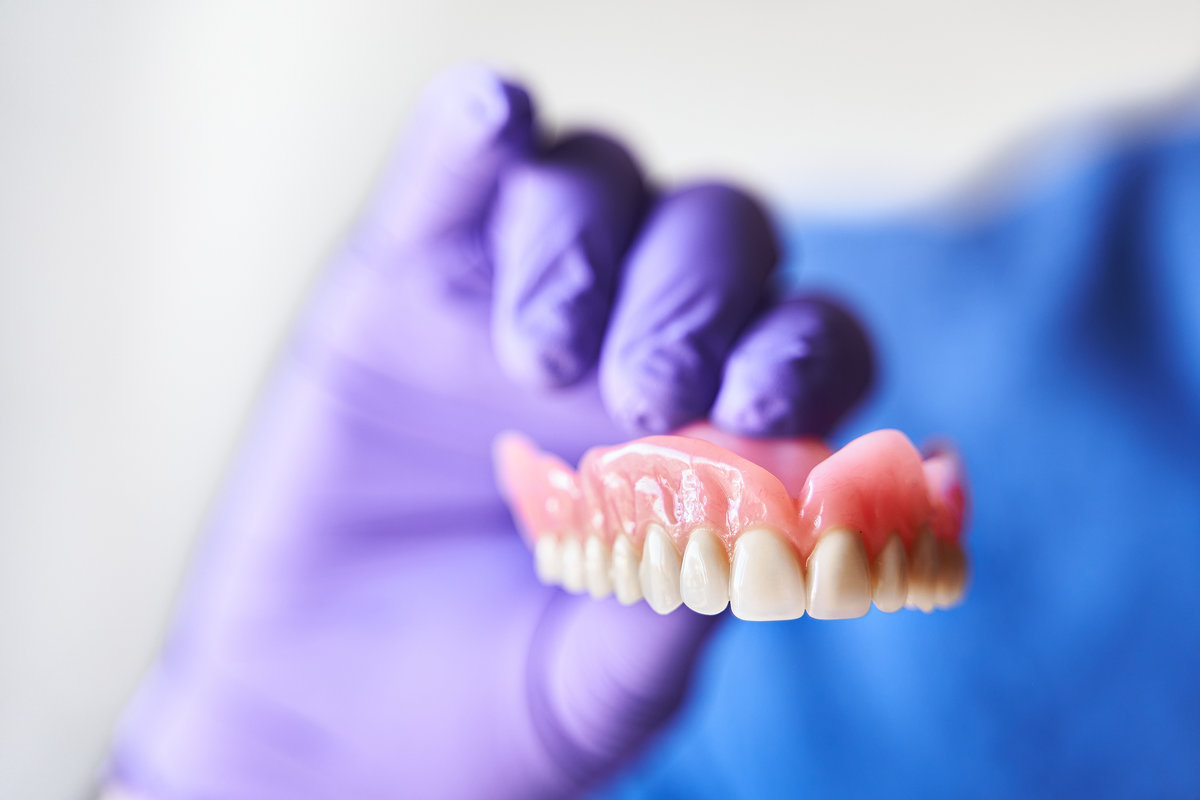 Dentist with purple gloves holding dentures in hand. Concept of dental prosthesis and dental health. Dentist with purple gloves holding dentures in hand. Concept of dental prosthesis and dental health.