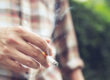 man holding smoking a cigarette in hand. Cigarette smoke spread in public areas outdoor. tobacco