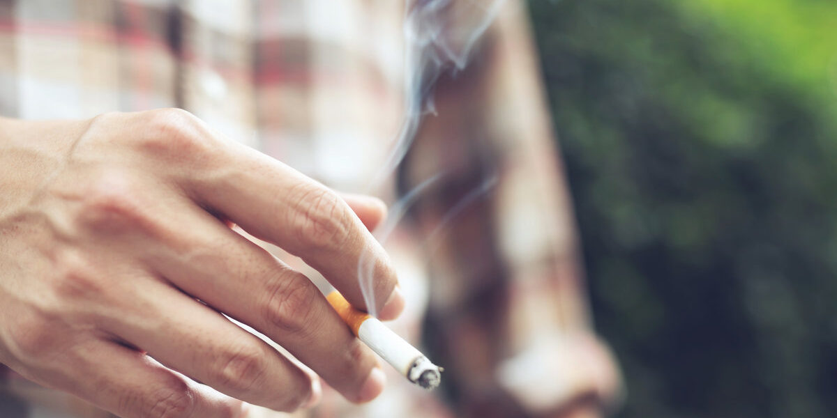 man holding smoking a cigarette in hand. Cigarette smoke spread in public areas outdoor. tobacco