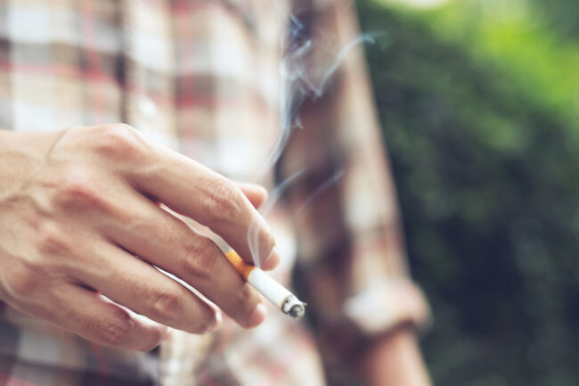 man holding smoking a cigarette in hand. Cigarette smoke spread in public areas outdoor. tobacco man holding smoking a cigarette in hand. Cigarette smoke spread in public areas outdoor. tobacco