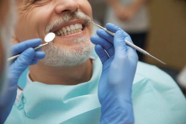 Smiling senior man with beard having a dental checkup with mirror and probe in a modern clinic Smiling senior man with beard having a dental checkup with mirror and probe in a modern clinic